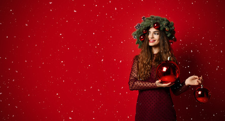 Beautiful woman with Christmas spruce fir wreath with cones and new year decoration balls on red 