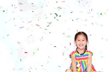 Obraz na płótnie Canvas Smiling little Asian kid girl with many falling colorful tiny confetti pieces on white background. Happy New Year or Congratulation Concept.
