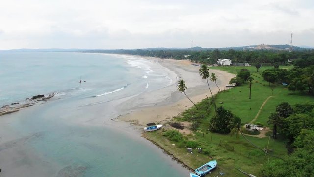 Aerial, drone shot, bypassing a Trincomalee city harbor, towards the sea, while waves hit the paradise beach, on a cloudy day, in Gokanna, in the Eastern Province of Sri Lanka, Asia