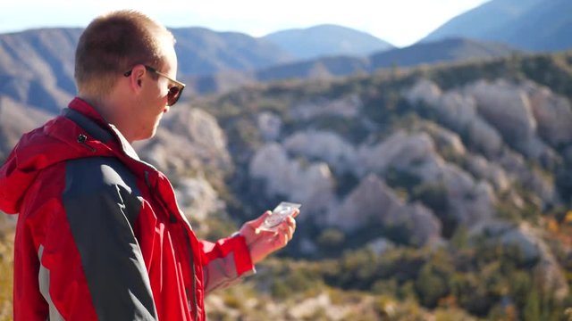 A man camping in the scenic California mountains holds a compass to navigate and find his location so that he does not get lost.