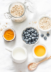 Ingredients for cooking coconut milk turmeric blueberry oatmeal porridge on a light background, top view. Gluten free, vegetarian food concept