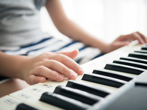 Boy playing keyboard piano near window at home.