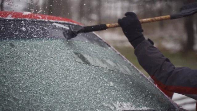 Man cleaning and scraping ice from car windshield in snow slowmo