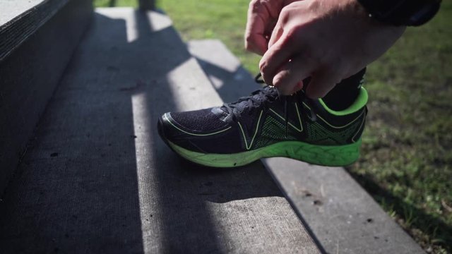 Slow motion close up of a man tying his athletic shoe on a wooden step