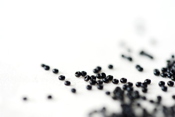 Seed beads of black color scattered on textile background close up