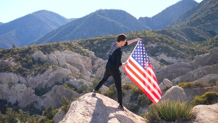 A young man patriot waving the red white and blue American flag above the California forest from an epic mountain peak in slow motion. - Powered by Adobe