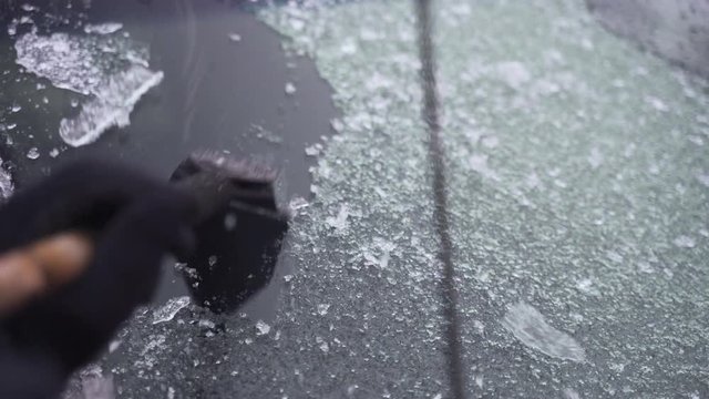 Man cleaning and scraping ice from car windshield in snow