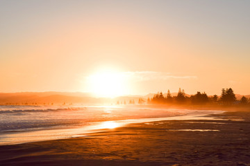 A pale orange sun setting on the beach landscape of Gisborne, New Zealand.