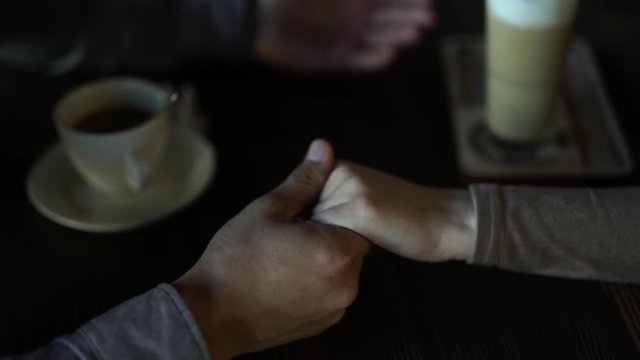 Couple/lovers sitting in a cafe. Man taking woman tender hands into his hands and holding them tightly. Love atmosphere. Couple/lovers under a table in a cozy cafe. There are a cup and glass of coffe