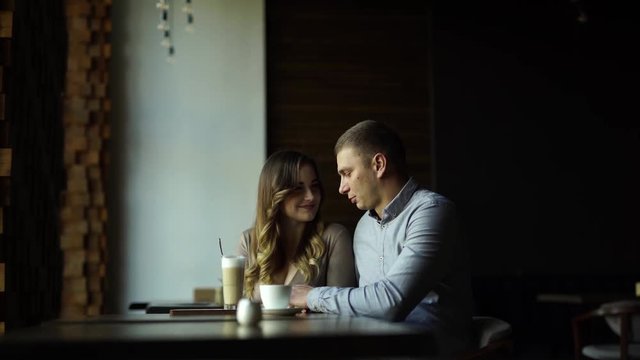 Beautiful blonde with wide beautiful smile and big breast/boobs in tight dress with decolette sitting in a cafe, posing to a camera phone of her man. There are a cocktail and a rose on a table