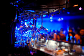 Empty wine glasses hanging over a bar rack in a nightclub. Dark background