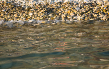 pebble stones on the sea beach, the rolling waves of the sea with foam
