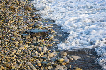 pebble stones on the sea beach, the rolling waves of the sea with foam