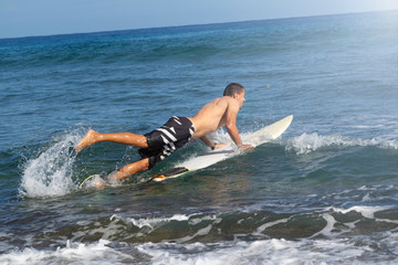 man lies down on a surfboard in the ocean. walks into the ocean.