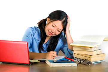 young happy and cute Asian Chinese student girl smiling happy working and studying with texbooks and laptop computer sitting on desk isolated on white background