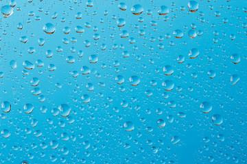 Macro shot of water drops with reflections on a window glass against turquoise blue background