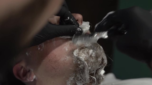 Tattoed hand of a barberman cleaning shaving blades by spraying them with special liquid to make them shiny and clean. Close-up concept