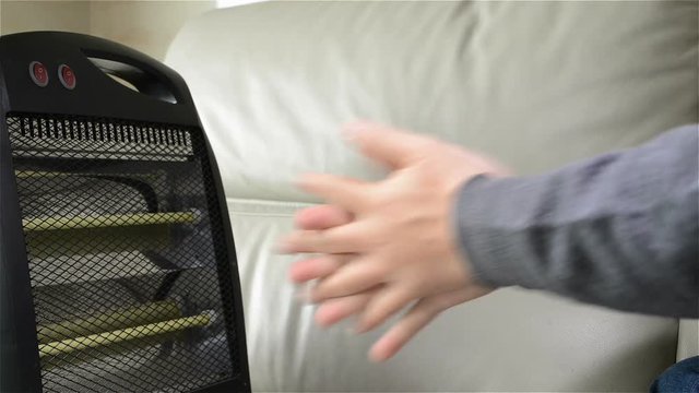 man turning on an electric heater at home to warm up his hands