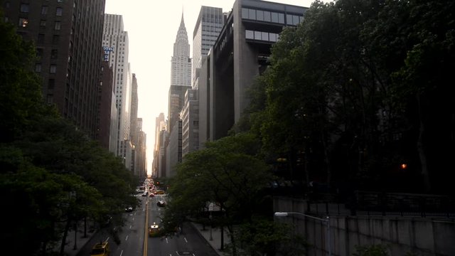 Looking down a busy New York City Street as vehicles try to get around under a beautiful sunset seen through the canyon of skyscrapers.