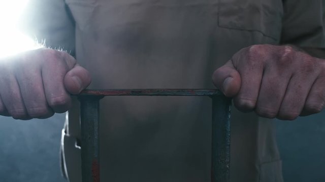 Extreme close-up parallax shot of a prisoner's hands holding onto the bars of his cell. When the camera stops moving, he walks off screen.