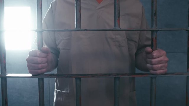Medium shot as a prisoner walks up, grabs the cell bars and then leaves after a beat.