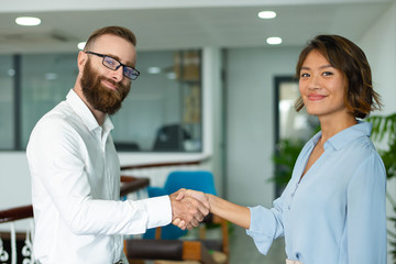 Obraz premium Content confident business partners making handshake and looking at camera. Smiling young multi-ethnic entrepreneur concluding deal. Startup business concept