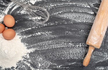 Home baking background with rolling pin flour and eggs on black background