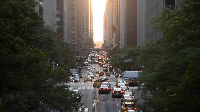 Looking down a busy New York City Street as vehicles try to get around under a beautiful sunset seen through the canyon of skyscrapers.