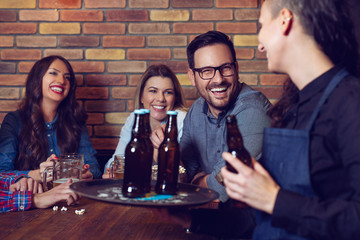 Cheerful group of friends joking and laughing with a waiter in pub.