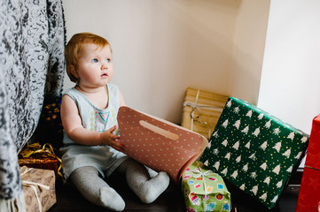 Portrait of a little girl in room sits and unpacks gifts. Festive birthday concept. Happy baby in photo. infant. International Women's Day, eighth of March. merry Christmas, happy holidays. new year.