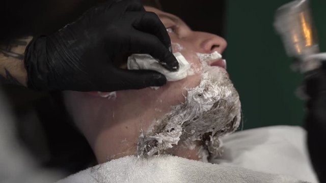 Tattoed hand of a barberman cleaning shaving blades by spraying them with special liquid to make them shiny and clean. Close-up concept