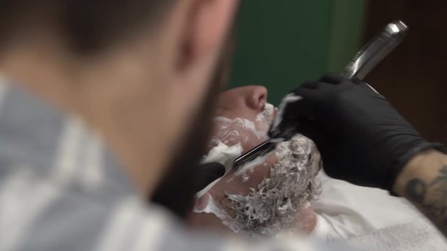 Tattoed hand of a barberman cleaning shaving blades by spraying them with special liquid to make them shiny and clean. Close-up concept