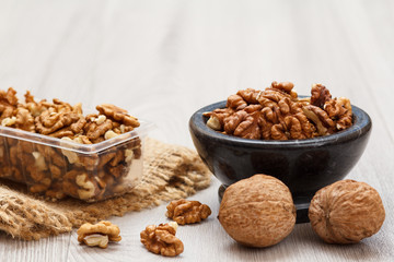 Walnuts in stone bowl and plastic container on a wooden background.