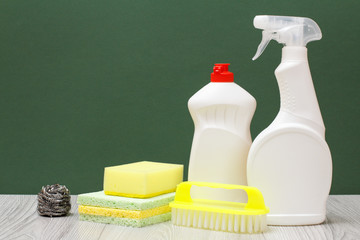 Bottles of dishwashing liquid, brush and sponges on green background.