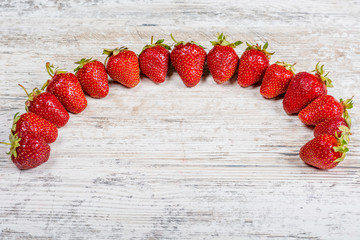 An arc of fresh ripe red strawberries lies on a light textured wooden table. Flatlay, Copyspace