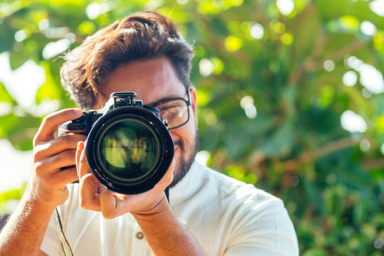 handsome and confident indian man photographer with a large professional camera taking pictures photo shooting on the beach.photo session on summer holiday on the background of green tropical trees