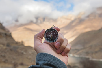 A male Hiker is looking for a direction with a magnetic compass in the mountains in the fall. Point of view shot. Man's hand with a watch bracelet holds a compass