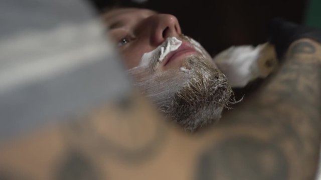 Customer's being applied shaving gel/cream in a barbershop. Client's covered with white peignoir. Close-up concept