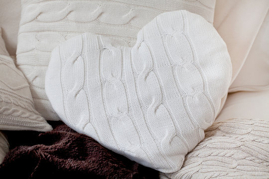 cosy heart-shaped knitted pillow with plait pattern on a couch