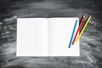 Color pencils, copybook on black board background. Back to school concept. 