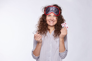 Fototapeta premium Pretty Caucasian female woke up early morning, wearing pajamas and sleeping mask, looks happy and stylish. Beautiful young woman realize that she is healthy and do not need medicine and pills anymore.
