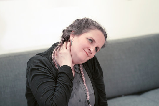 Tired neck. Woman suffering from neck pain at home on couch. A woman's sense of fatigue, exhausted, stressed. A girl massages her painful neck with her hands. The concept of body and health.