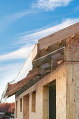 Vertical photo of small wooden house without windows and doors. Construction new building with wooden beams on the roof and wall OSB panels