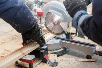 Close up photo of two unrecognizable man using hand electric saw mill to cut part of wooden block