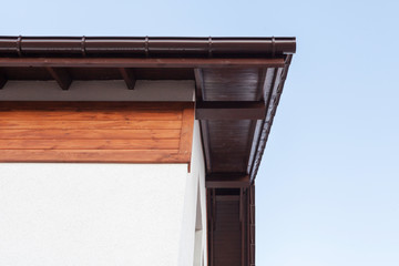 Close up low angle top view photo of brown roof corner with wooden elements on top of small comfortable house with white walls © brizmaker