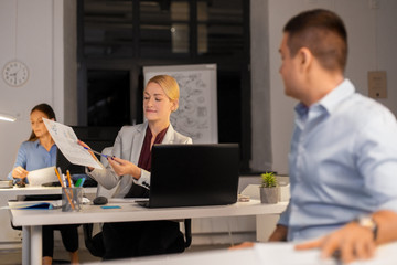 business, deadline and technology concept - woman showing charths to colleague late at night office