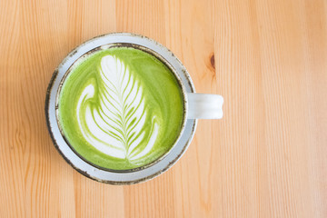Matcha green tea latte in a cup on wooden table background.Hot Matcha coffee latte with beautiful milk foam latte art texture.