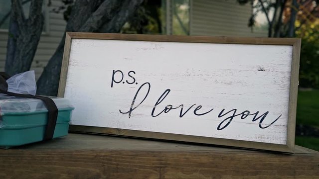 A wooden sign that reads "p.s. I love you" at an outdoor summer wedding reception.