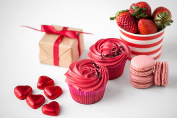 valentines day and sweets concept - close up of frosted cupcakes, red heart shaped chocolate candies, macarons, strawberries and gift box