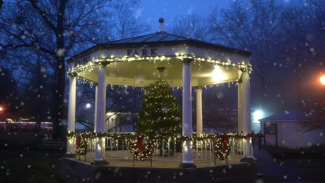 Snowing scene of charming rotation of a gazebo in a state park in Berkeley Springs, WV with a christmas tree lit up in the evening.